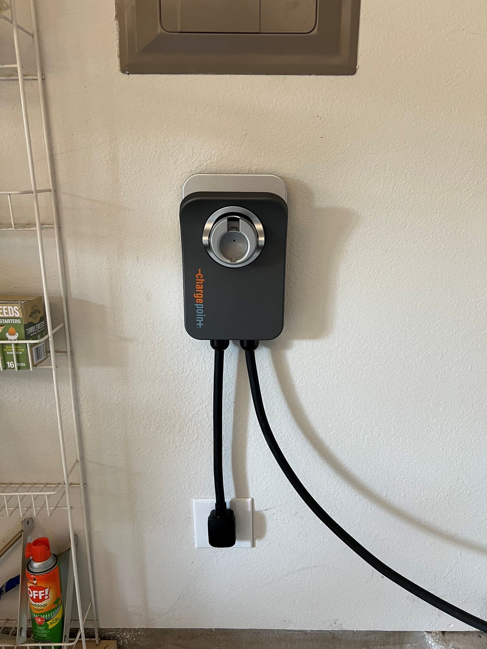 EV charger mounted on a wall, with a black cable and plug connected to an outlet.