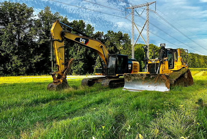 Yellow excavators clearing grass in a field near power lines on a sunny day