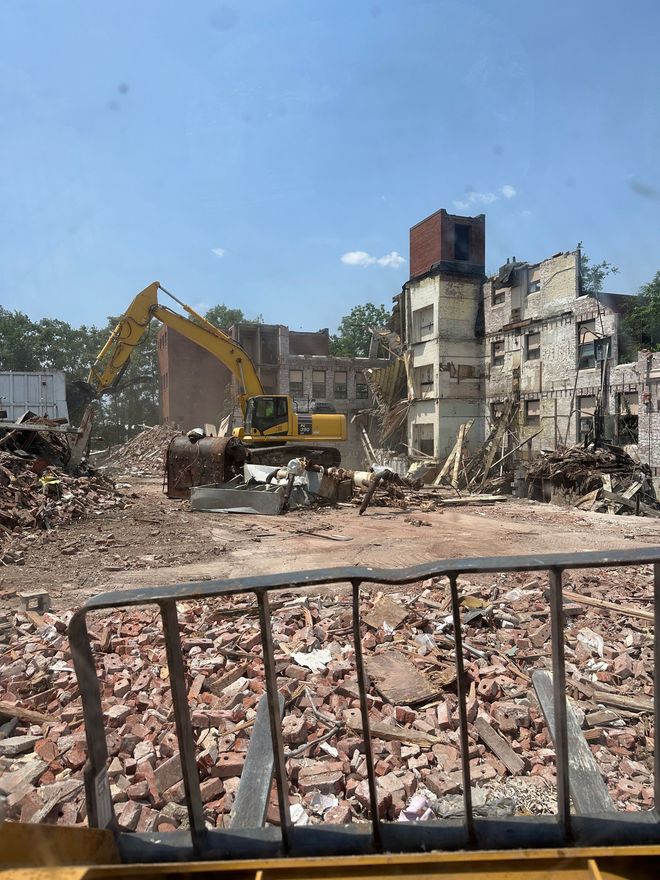 Demolition site with an excavator amid rubble and damaged buildings under a blue sky