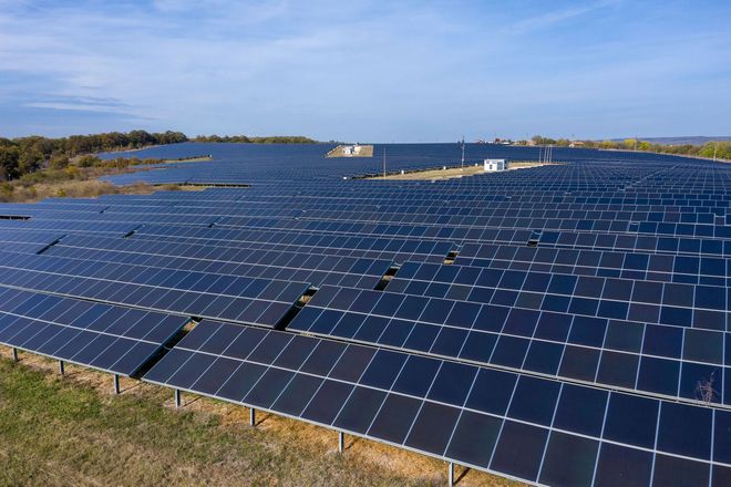 Solar panels covering a large field under a blue sky near water