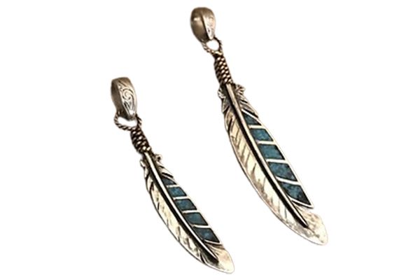 A pair of silver feather pendants on a white background