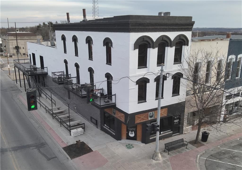An elevated view of a white, three-story building with black trim, street-level storefronts, and an outdoor patio area.