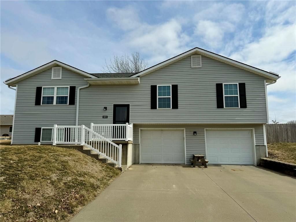A light gray, two-story split-level house with white trim, two garage doors, and a front porch with a white railing.