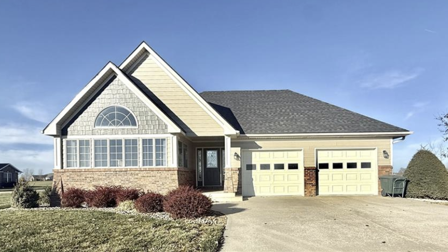 Suburban house with beige siding, a two-car garage, and a landscaped front yard under a clear sky