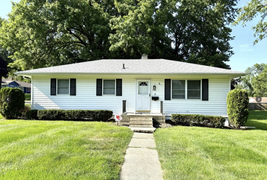 White ranch-style house with black shutters, steps to the front door, and green lawn.