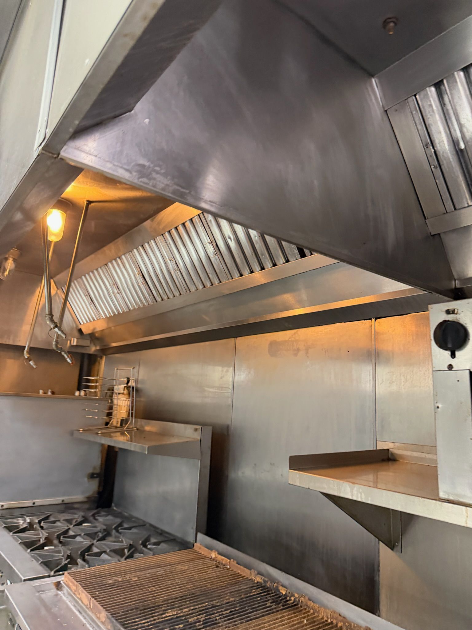 Commercial kitchen with stainless steel hood, prep counter, and grill equipment under warm lights