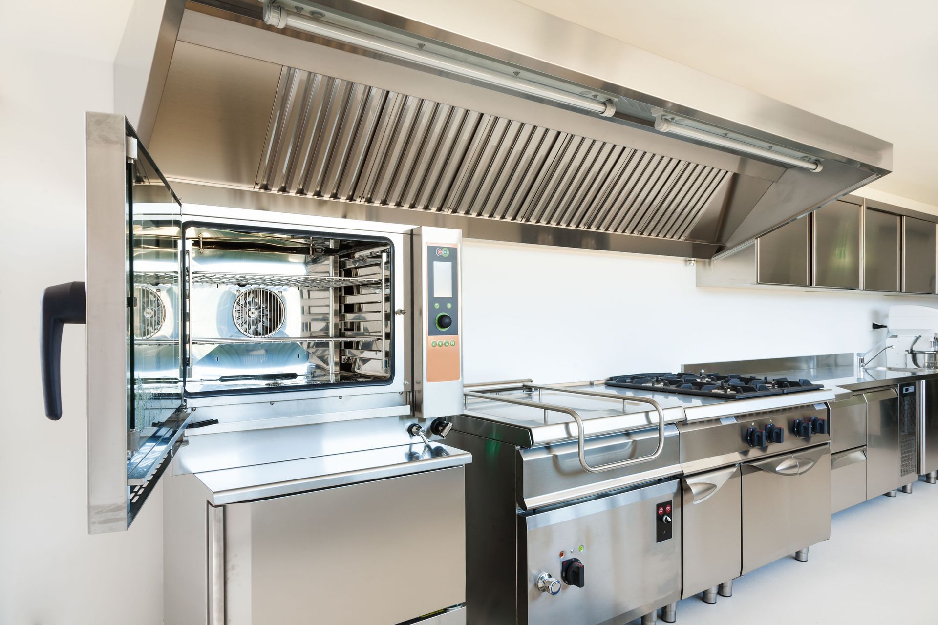 Commercial kitchen line with stainless steel appliances, grill, oven, and large ventilation hood