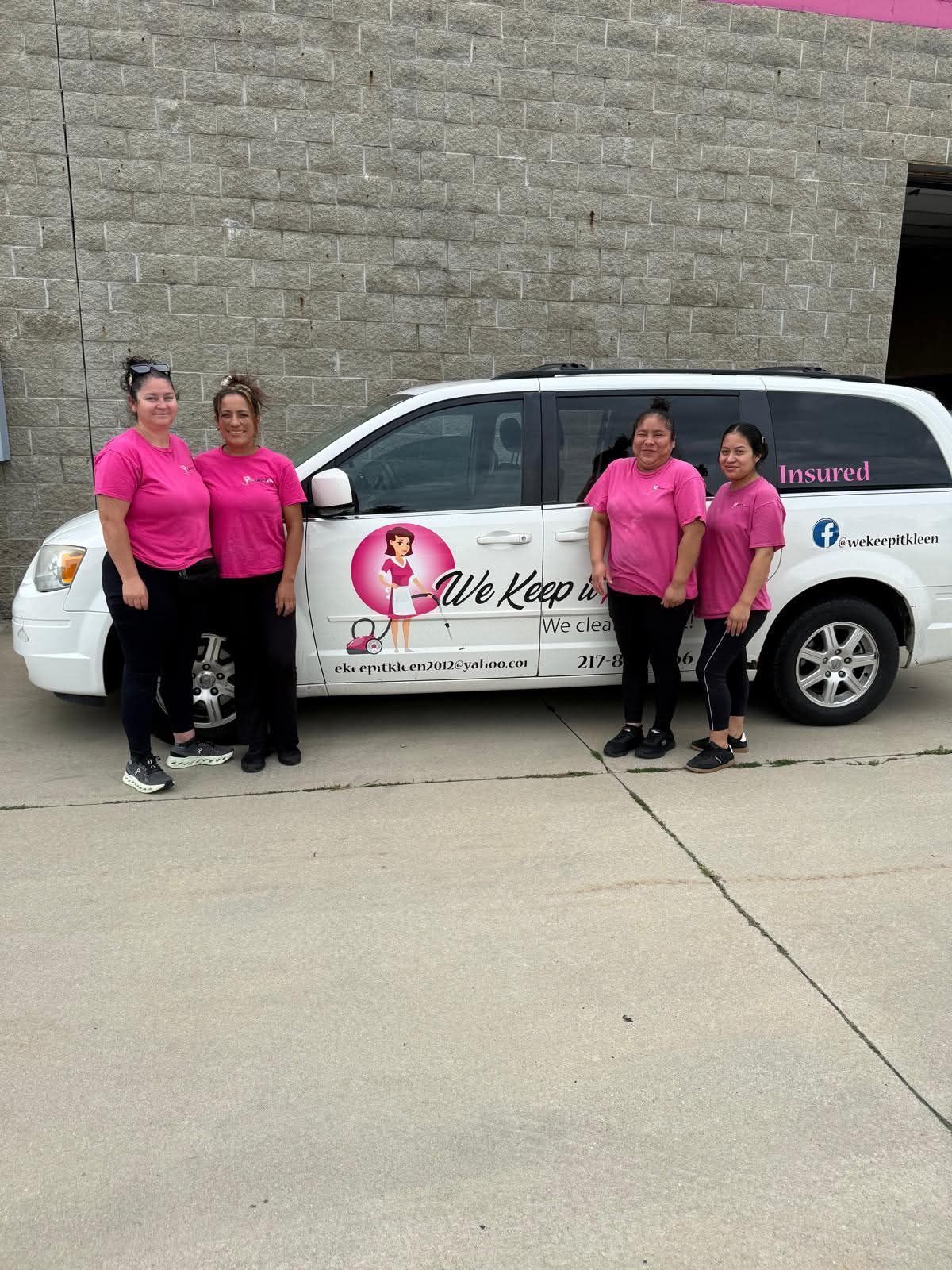 Four people in pink shirts stand beside a branded white van outside a brick building.
