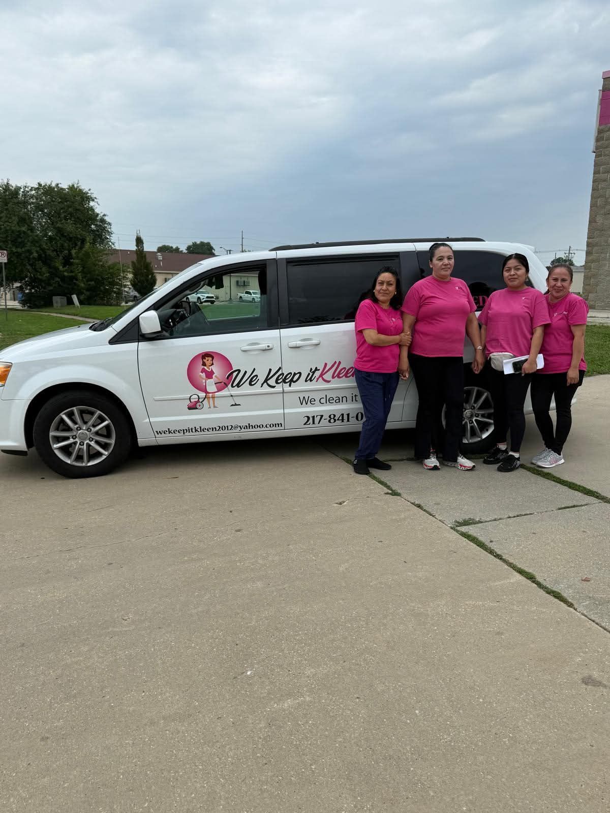 Four people in pink shirts standing beside a white van with a logo in a parking lot.