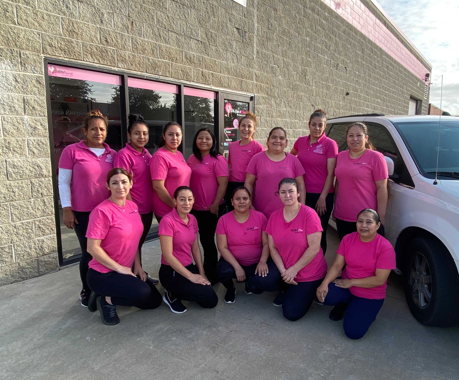 Group of women in pink shirts pose outside a building.