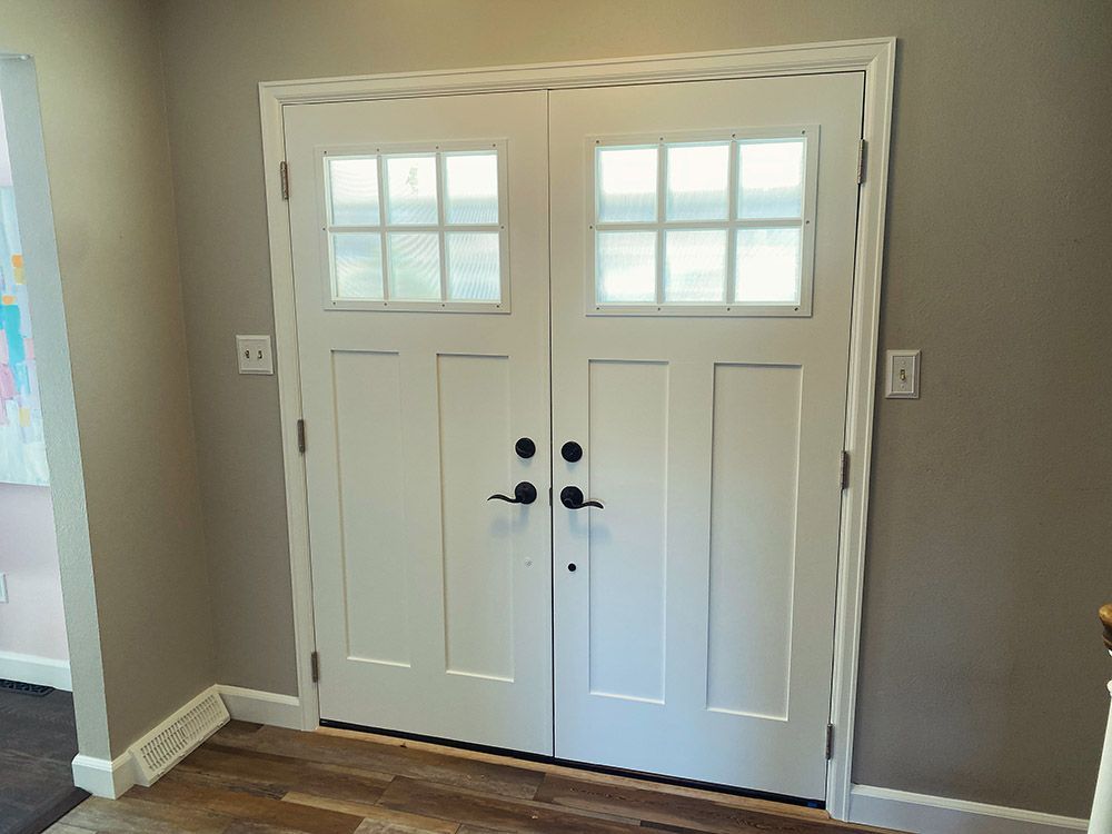 a pair of white doors with square windows in a hallway.