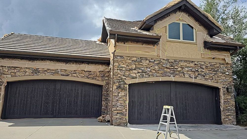 a large house with two garage doors and a ladder in front of it.