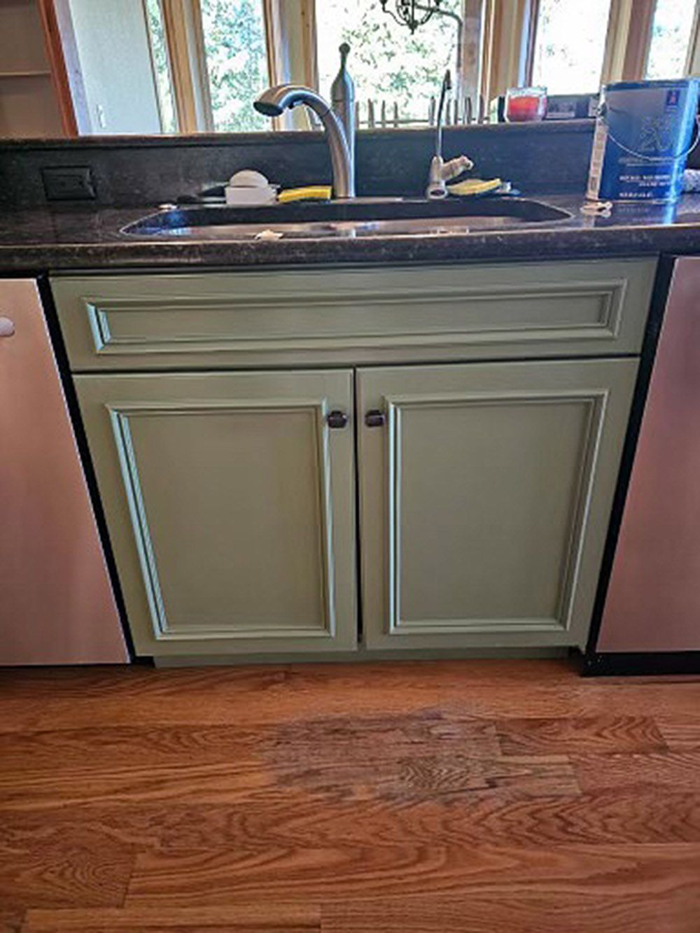 a kitchen sink with green cabinets and a stainless steel faucet.
