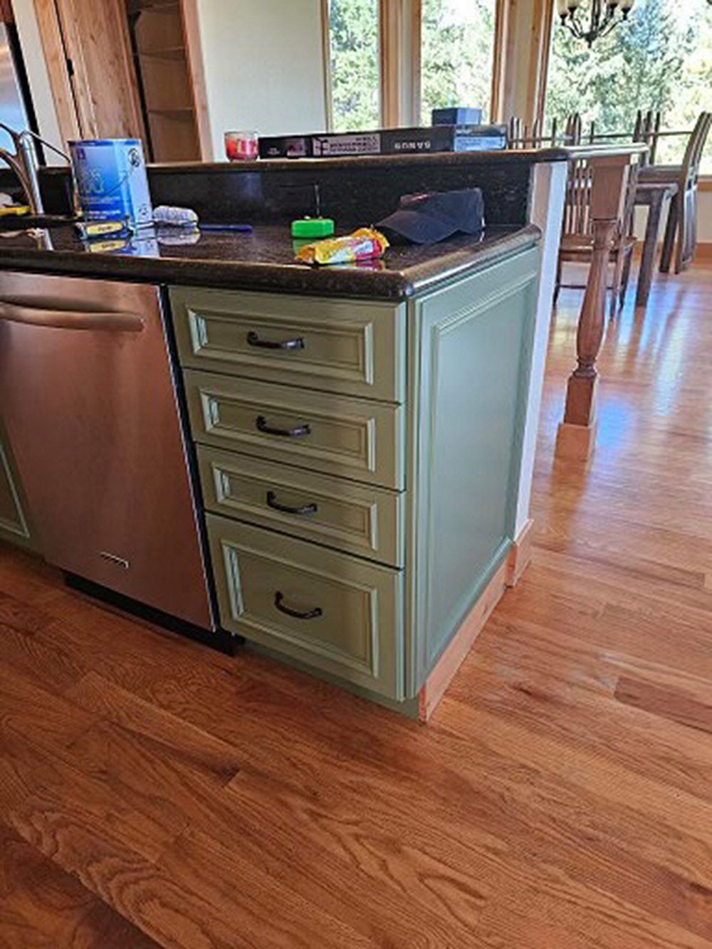 a kitchen with green cabinets, a stainless steel dishwasher, and a wooden floor.