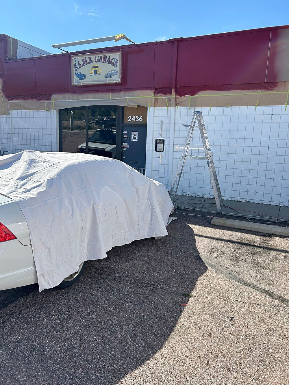 a white car is parked in front of a building that is being painted.