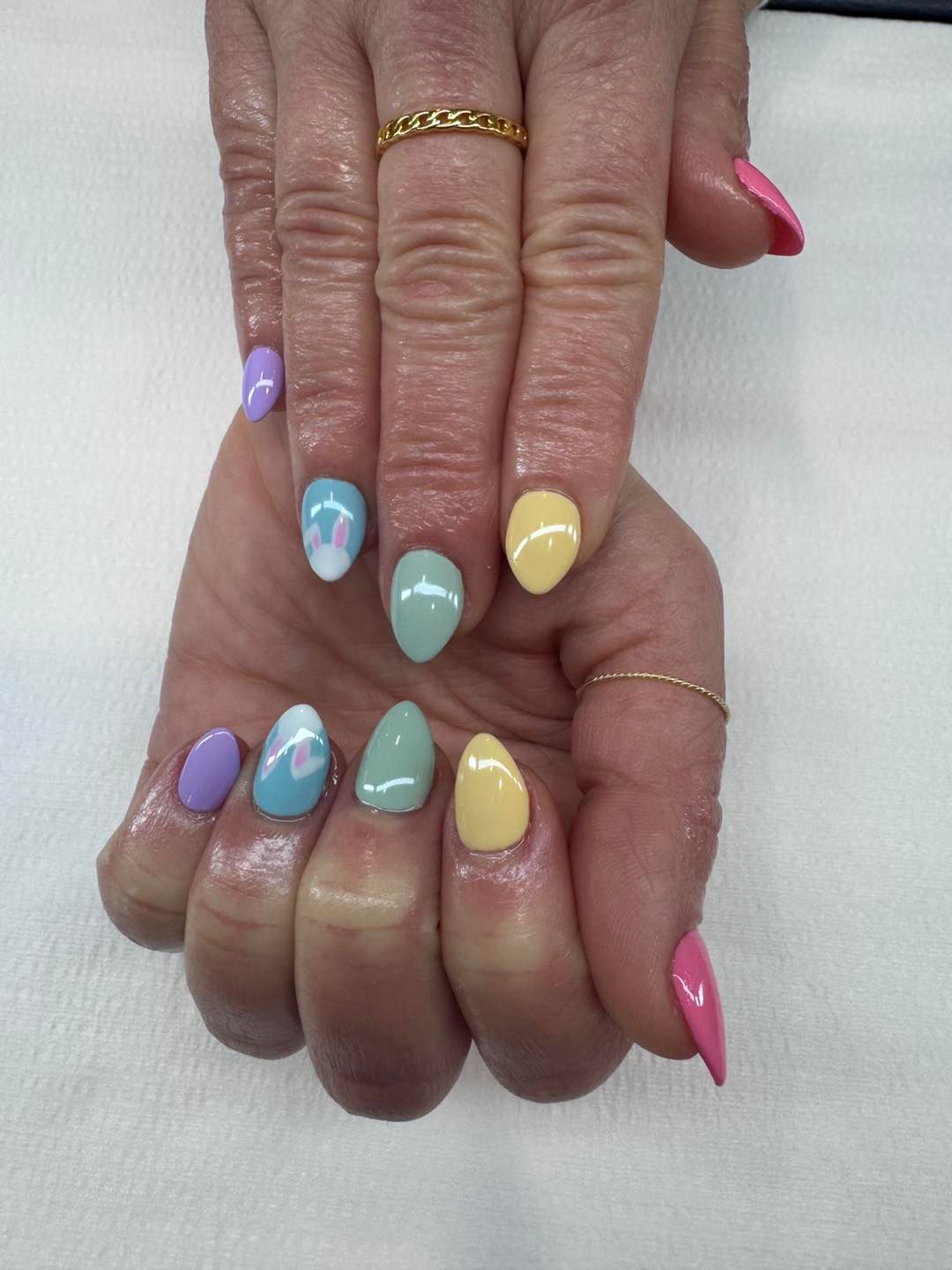 Woman's hand with almond-shaped nails in pastel colors. Some have white flower accents, one has a gold ring.