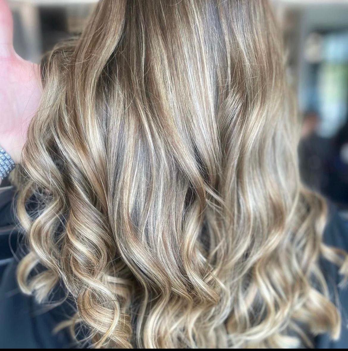 Woman with wavy, highlighted hair: blonde, brown, and tan shades, styled in layers.