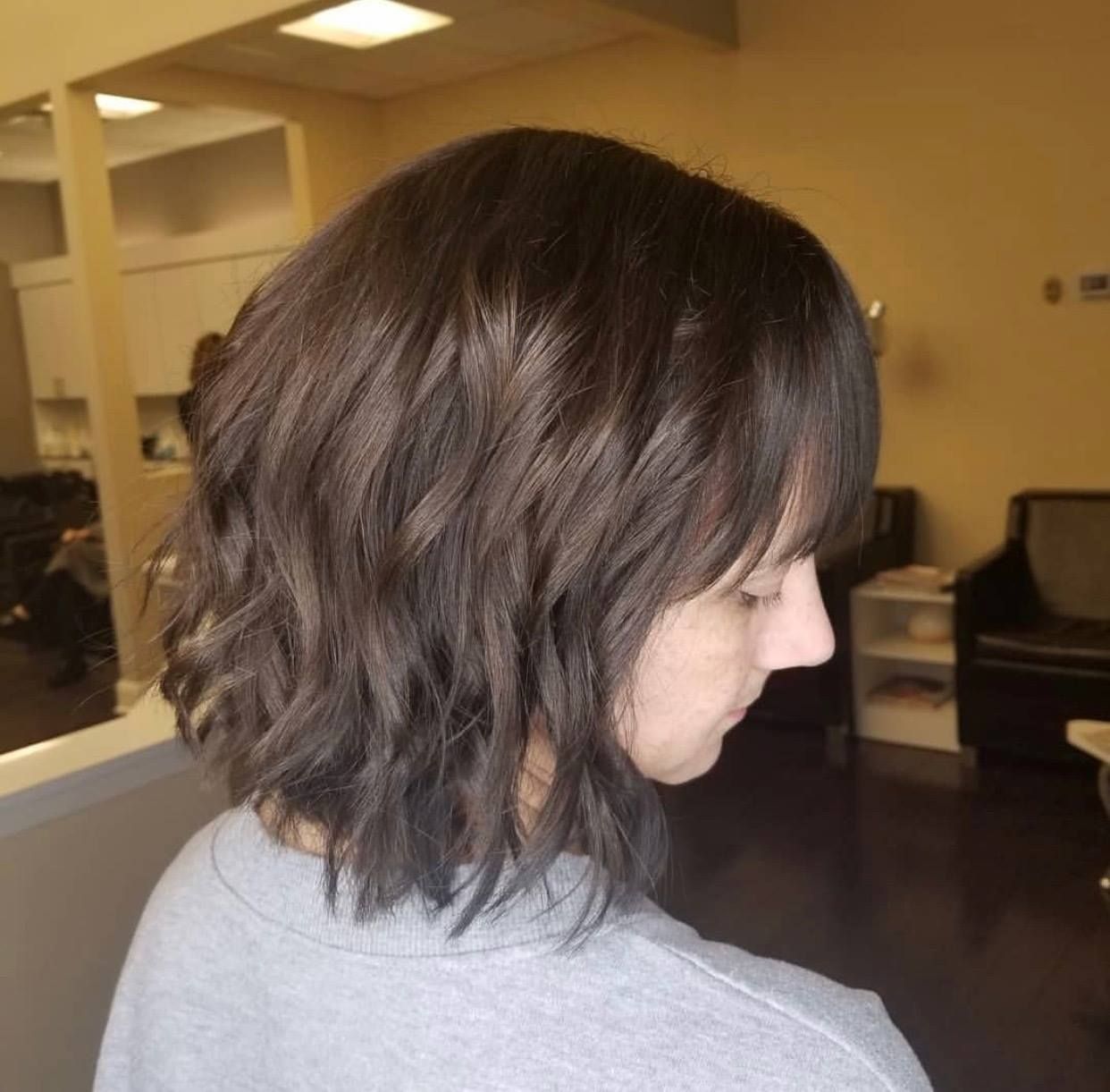 Woman with wavy dark hair, short bangs, and gray shirt, in a salon.