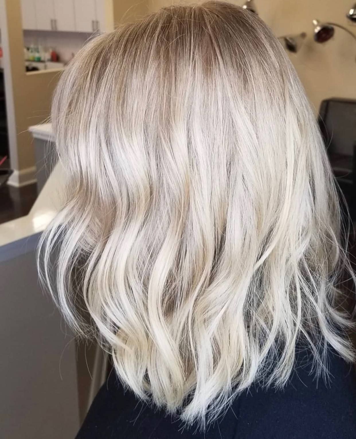 Blonde shoulder-length wavy hair with darker roots, in a salon setting.