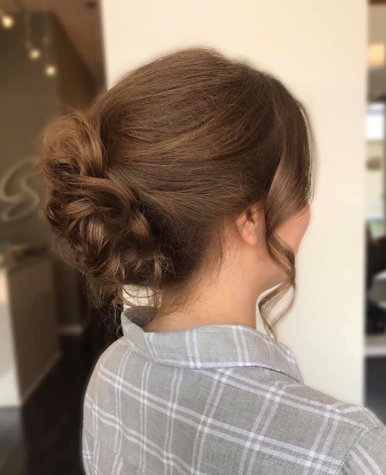 Woman with brown hair in an updo. Loose strands frame the face. Wearing a gray plaid shirt.