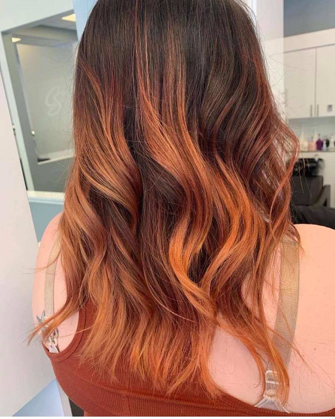 Woman with wavy auburn hair, dark roots, and copper highlights in a salon setting.