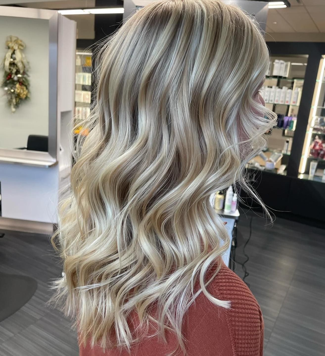 Woman with wavy blonde hair, highlights and lowlights, indoors in a salon setting.