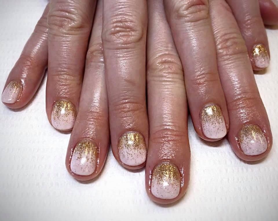 Hand with nails painted with pink and gold glitter ombre.