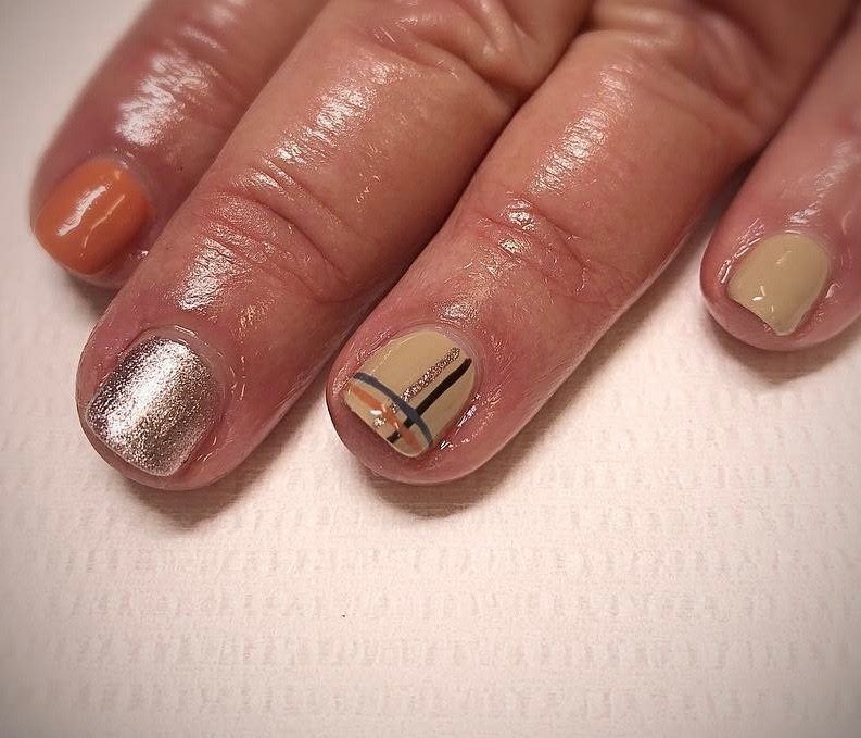 Close-up of a hand with nail polish in muted orange, silver glitter, beige, and a design with black lines.