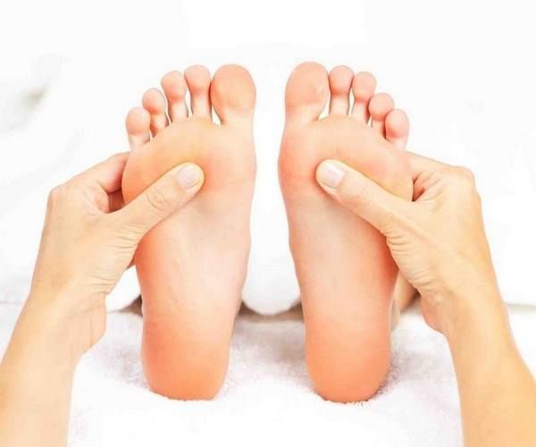 Hands massaging the soles of two feet, on a white surface.