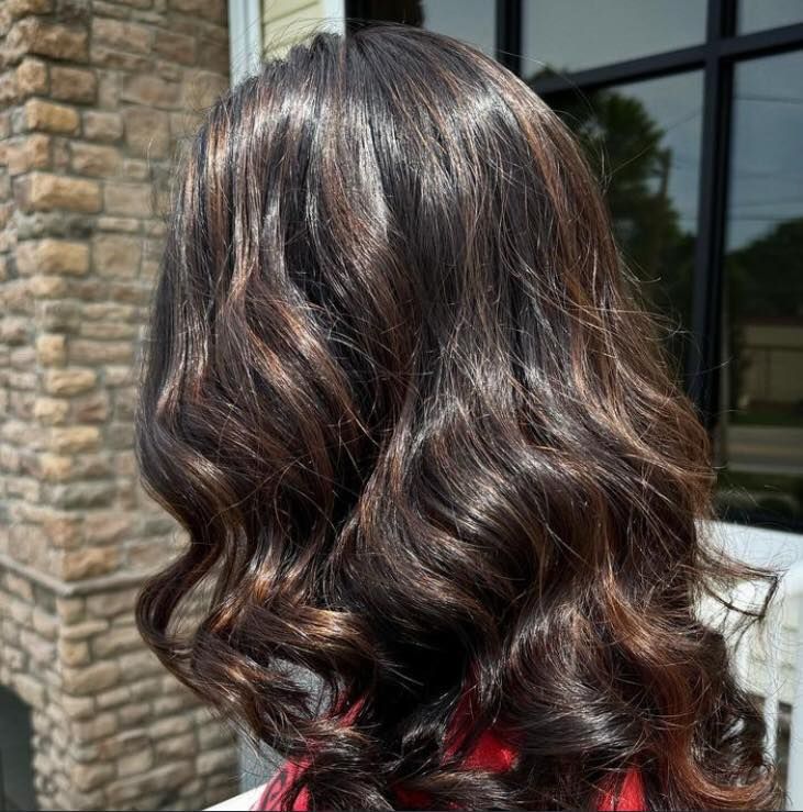 Woman with dark brown, wavy hair with highlights, outside in sunlight.