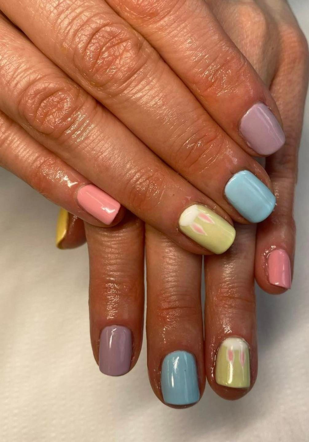 Hands with pastel-colored square-shaped manicured nails: pink, purple, yellow, and blue.