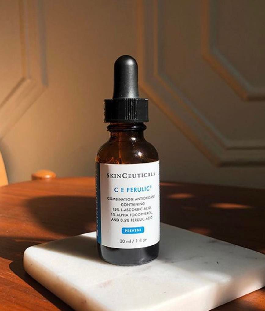 Brown glass bottle of SkinCeuticals C E Ferulic serum with a dropper, on a white marble slab, bathed in sunlight.