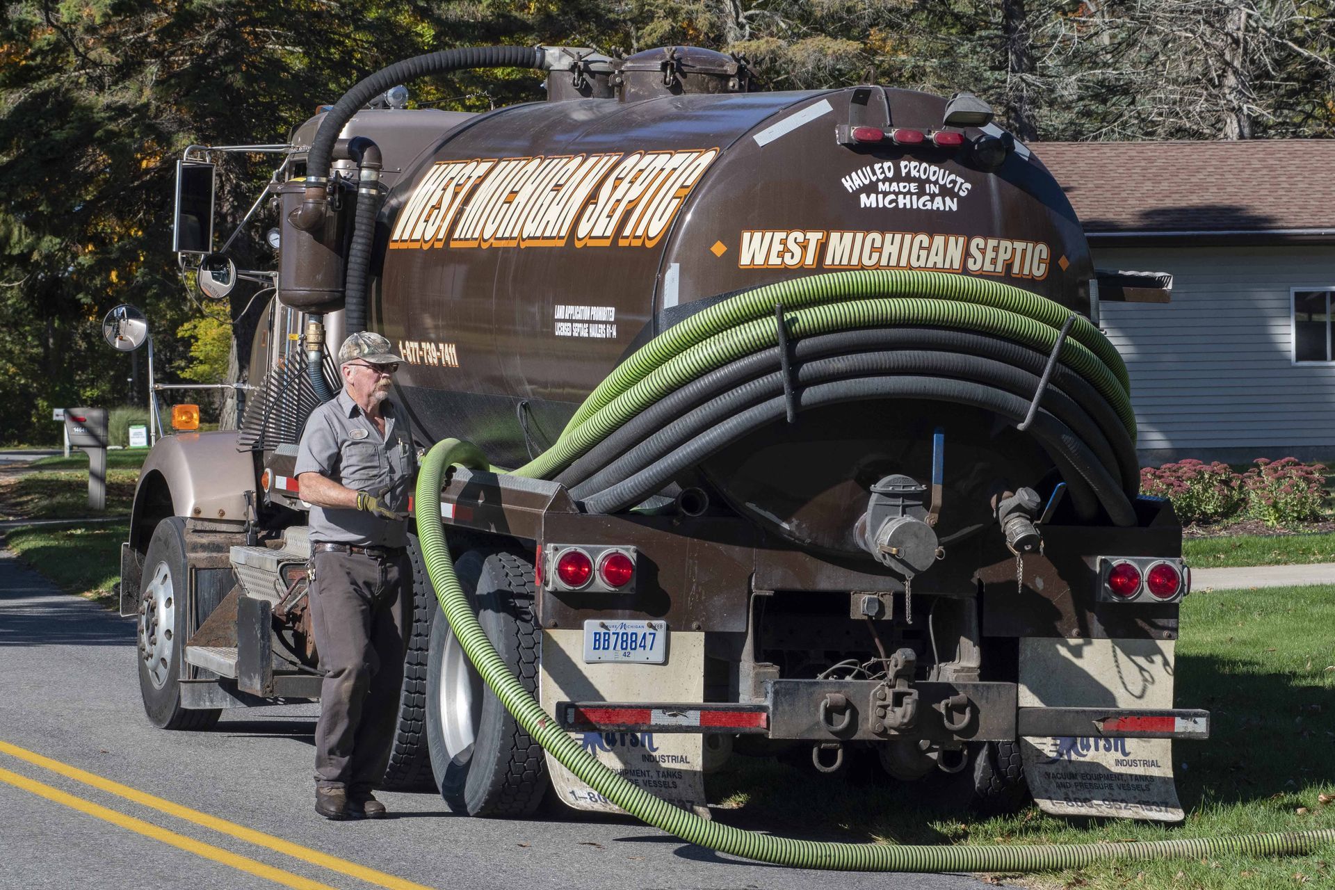Septic truck parked on the street, a worker attending to a green hose.