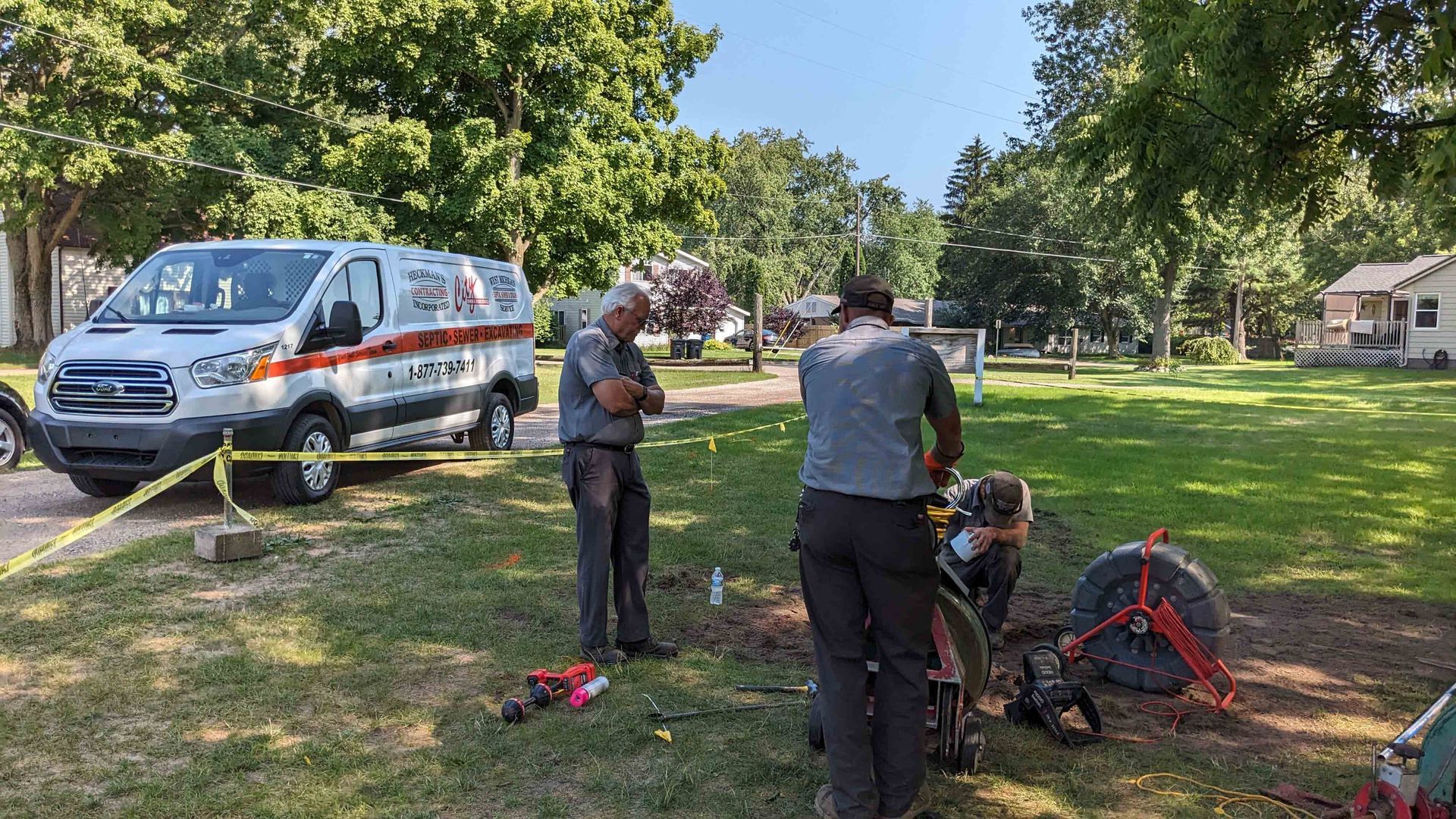 Two men examine a bicycle near a medical van on a sunny, grassy lawn. Yellow caution tape is present.