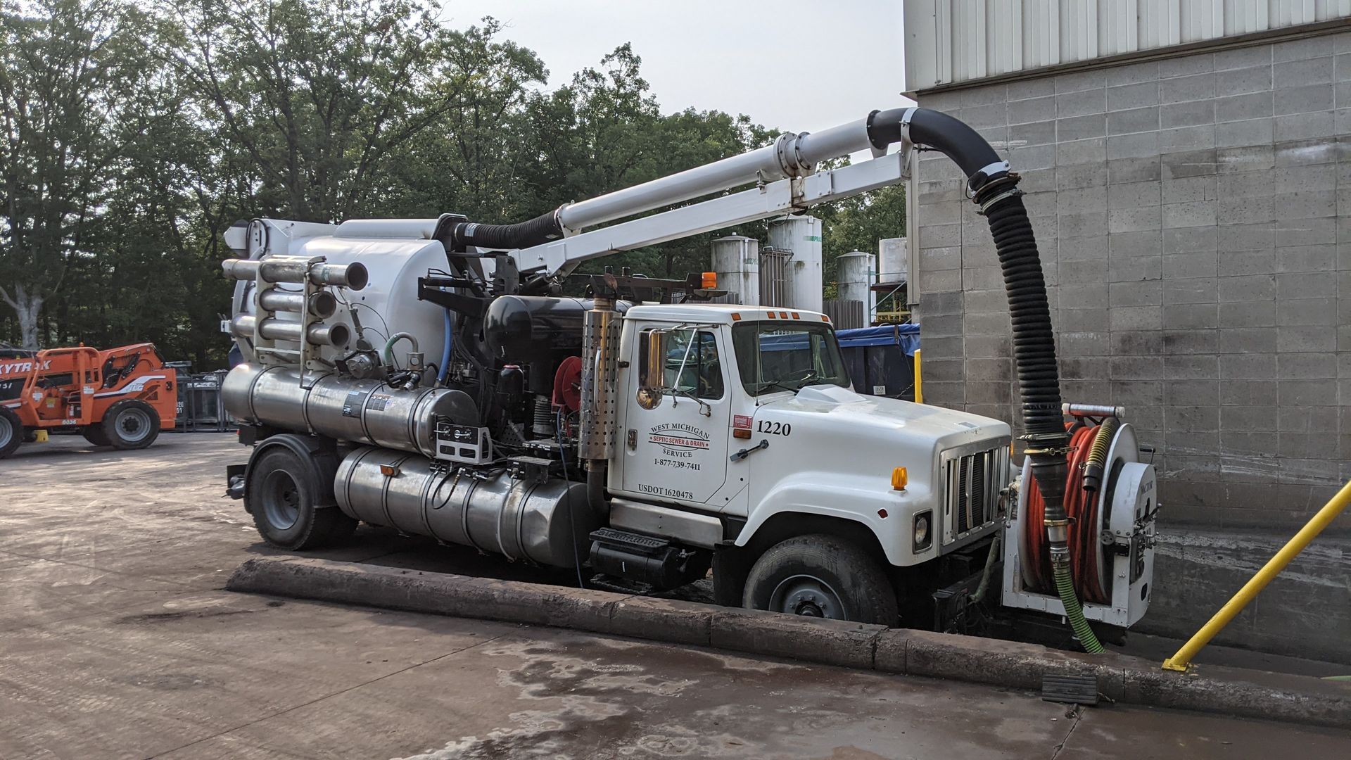 White vacuum truck, with extended arm and hose, next to a concrete wall.