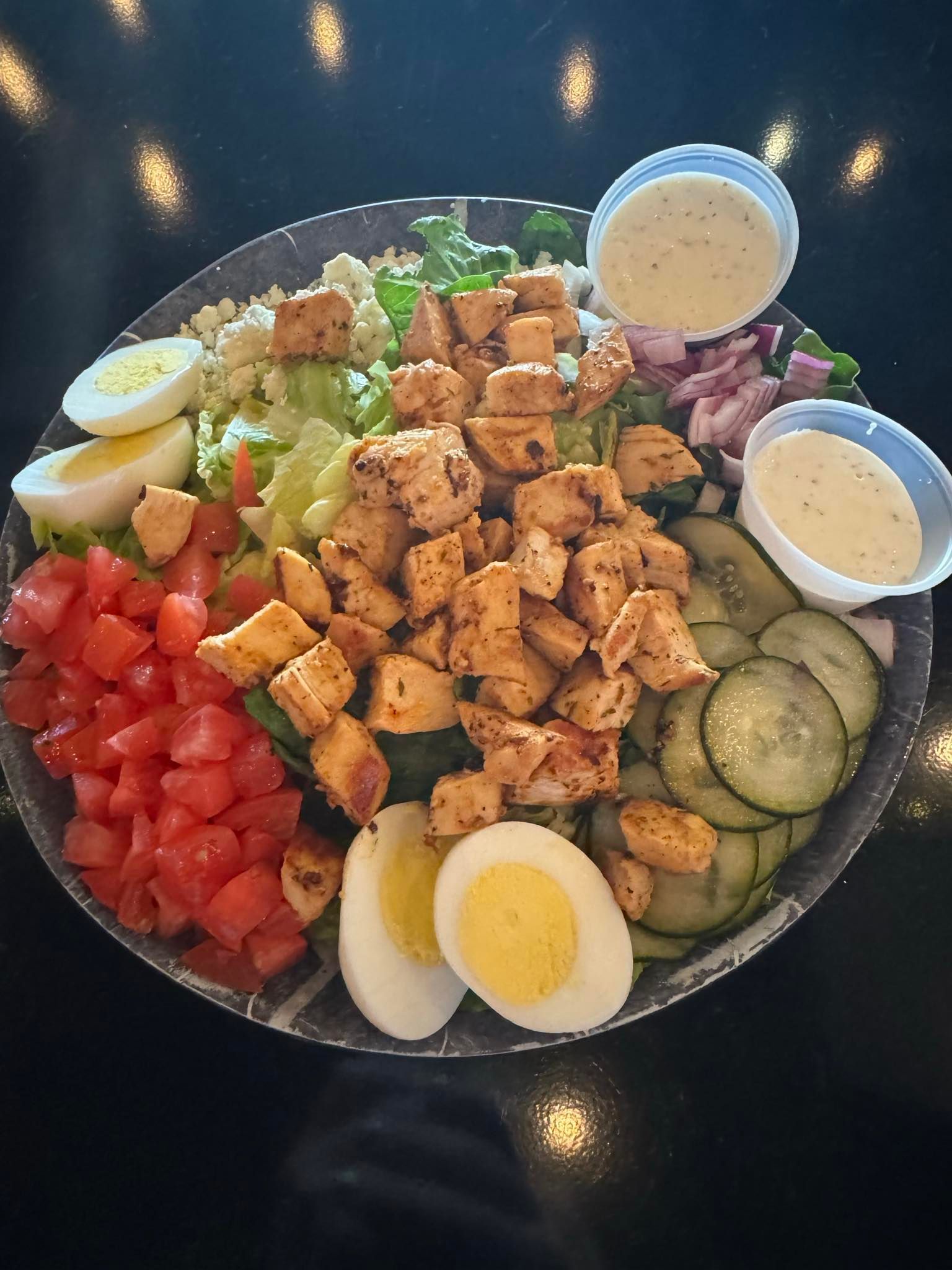 A salad with chicken , eggs , cucumbers , and tomatoes on a plate on a table.