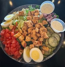 A salad with chicken eggs tomatoes and cucumbers on a plate
