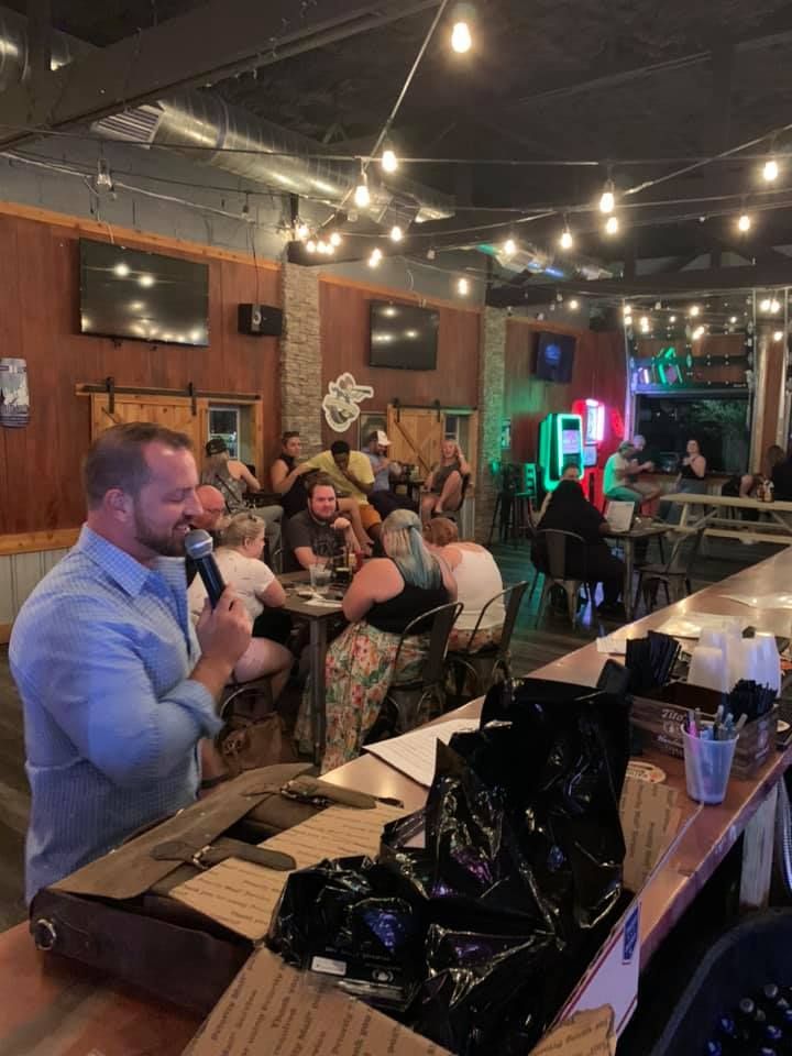 A man is holding a microphone in front of a crowd of people in a restaurant.