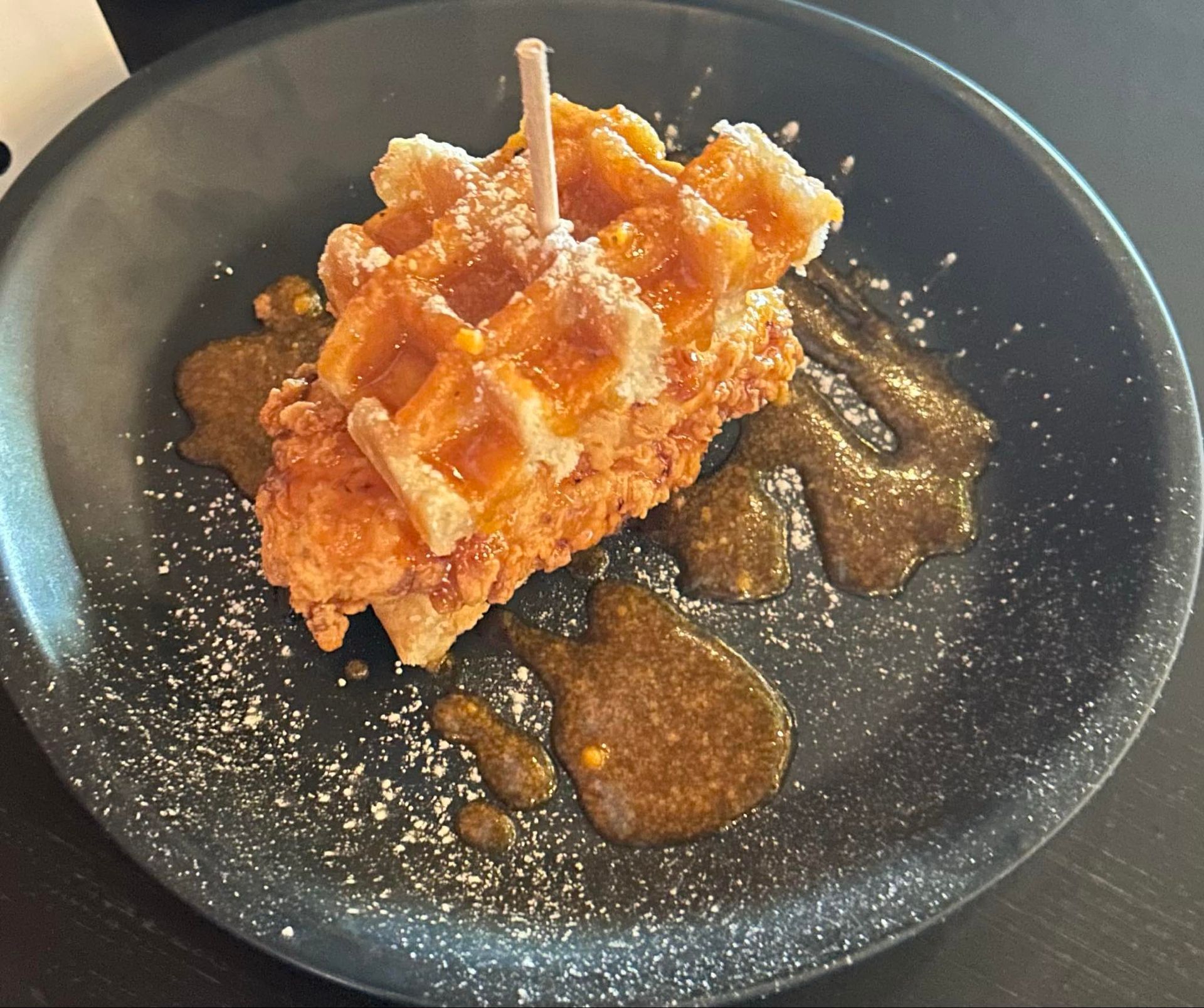 A black plate topped with a waffle and syrup