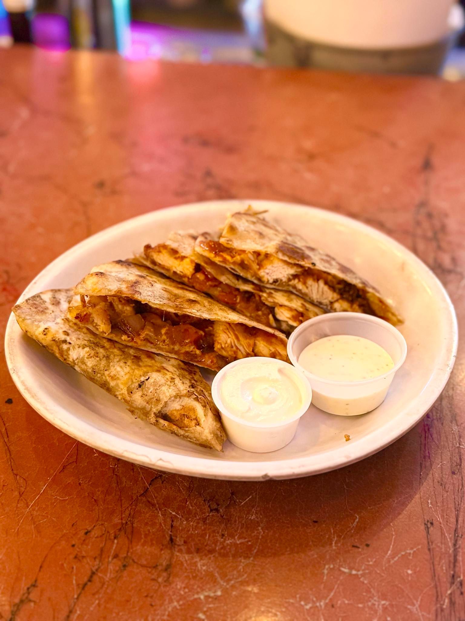 A plate of quesadillas with dipping sauces on a table.