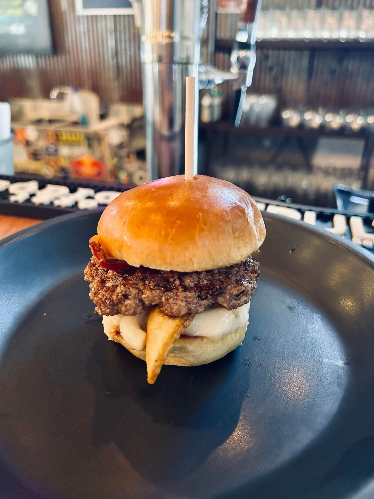 A small hamburger on a black plate with a toothpick in it.