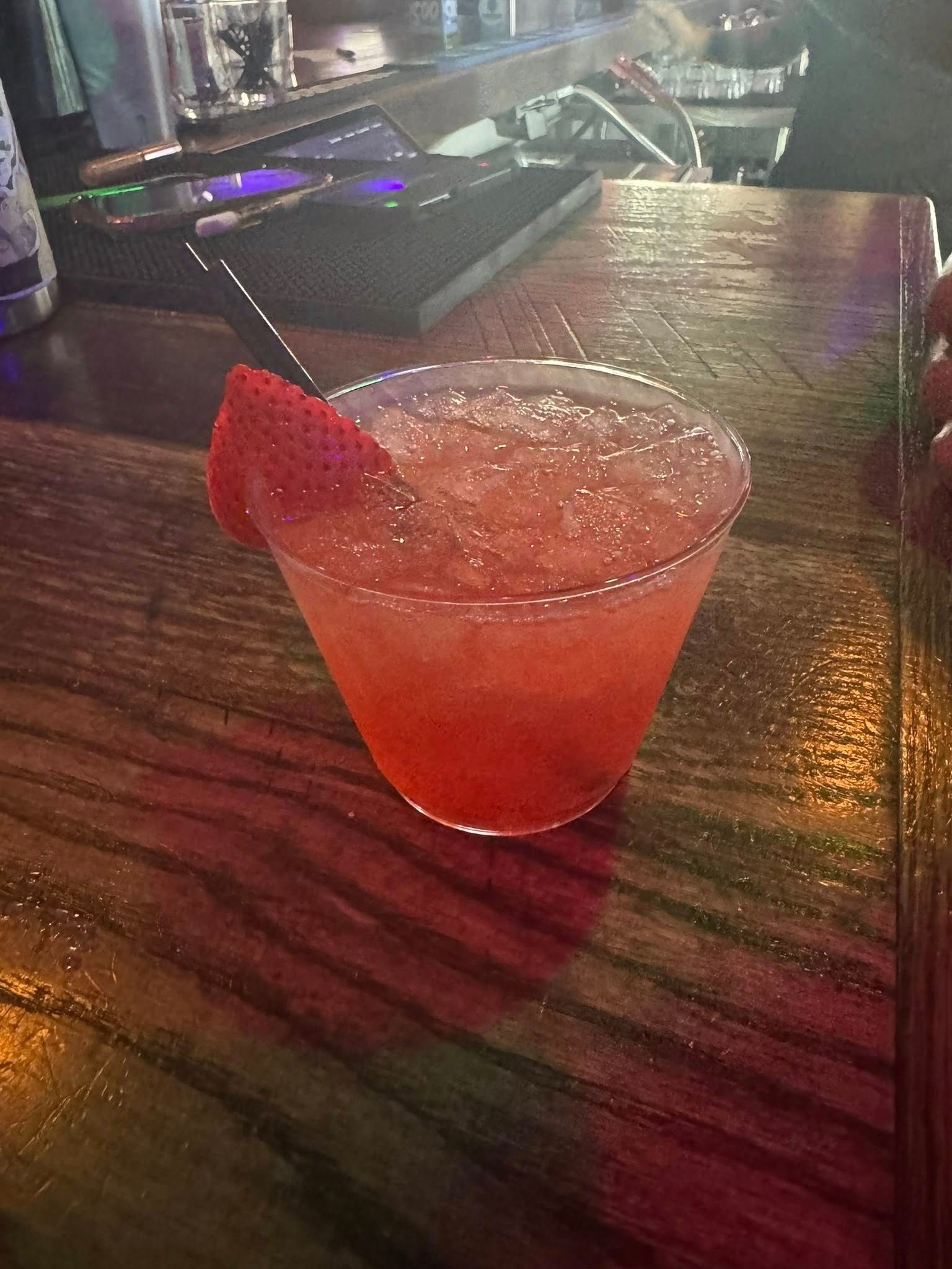 A red drink with a straw in it is on a wooden table.