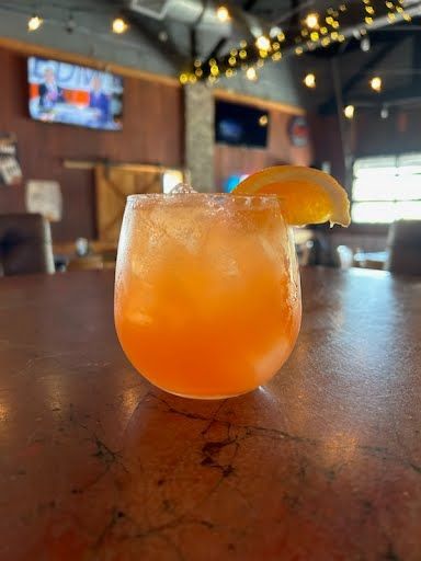 A close up of a drink with a slice of orange on a table.