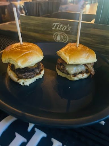 Two sliders on a black plate with toothpicks in them.