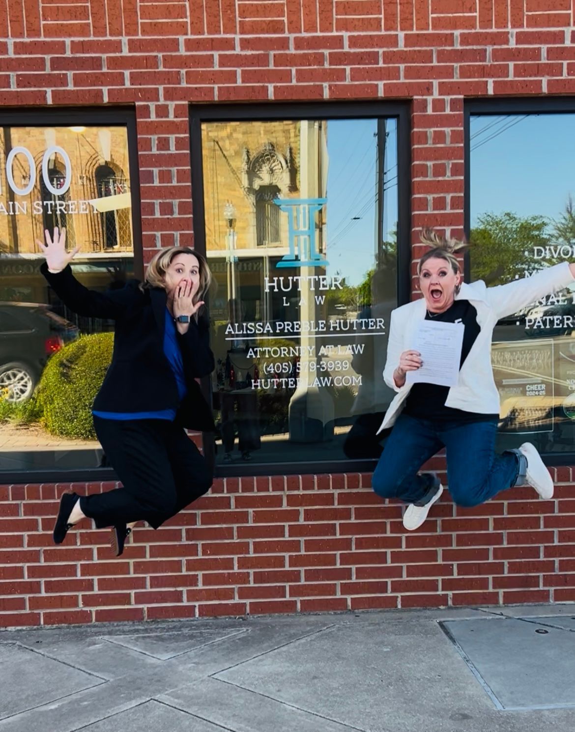 Two women are jumping in the air in front of a brick building