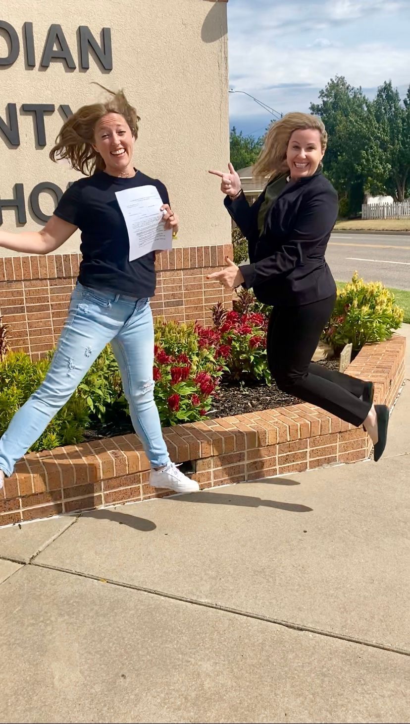 Two women are jumping in the air in front of a building.