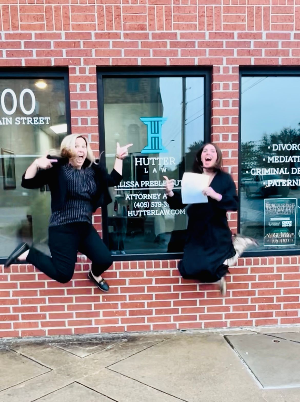 Two women are jumping in the air in front of a brick building