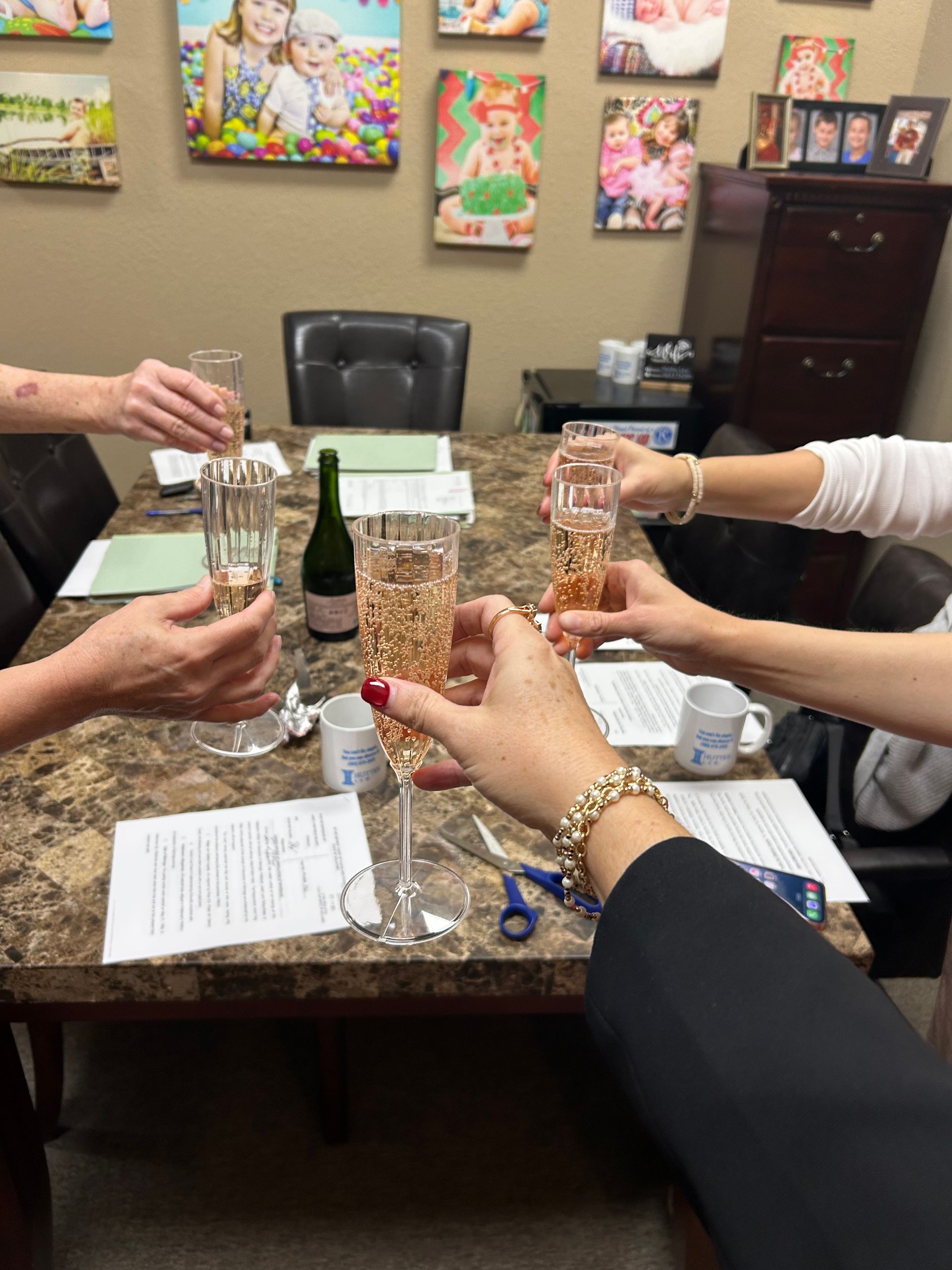 Five people toasting with champagne flutes around a table with paperwork.