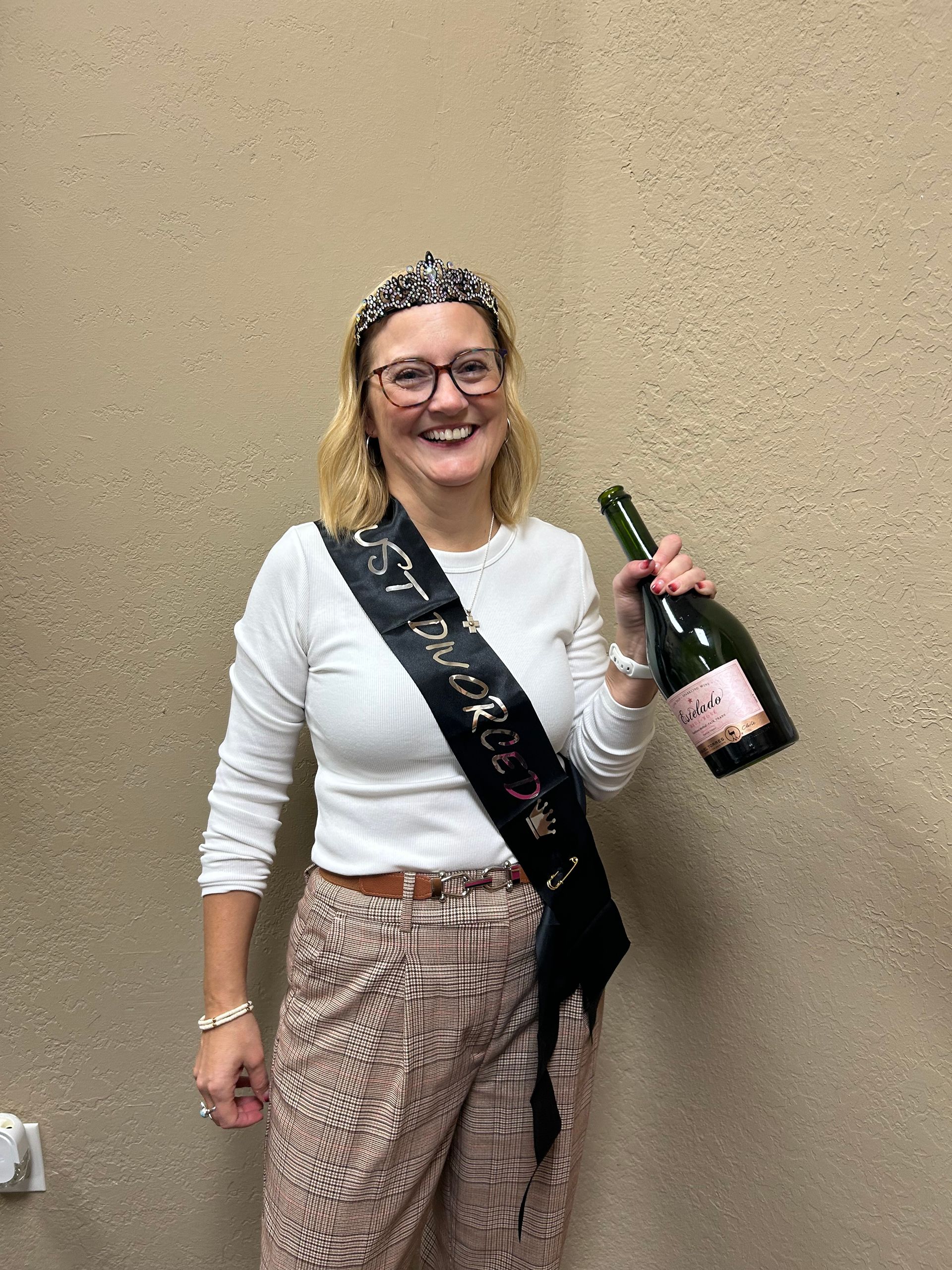 Woman wearing  Just Divorced sash, holding a champagne bottle, smiling.