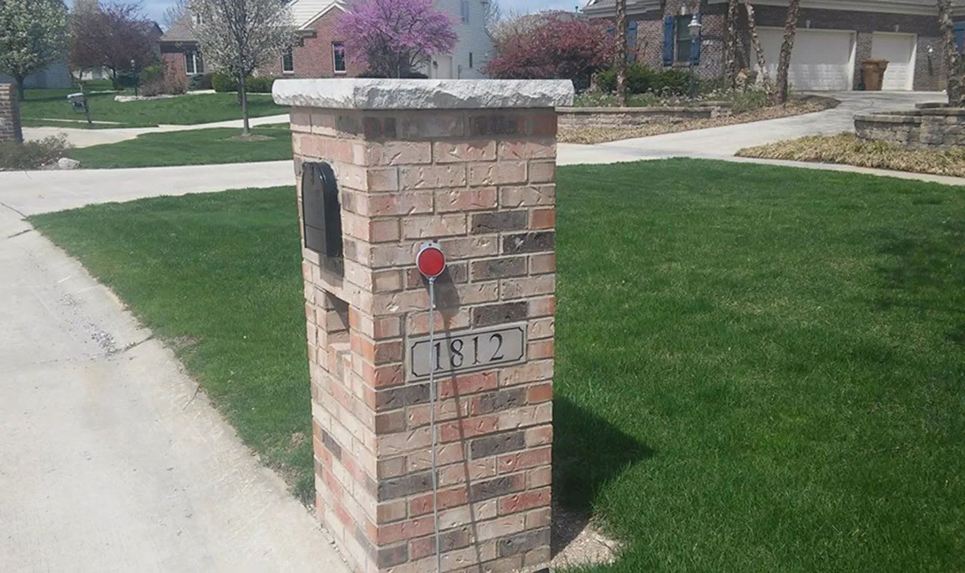 Brick mailbox with address numbers, a light, and a black mail slot on green lawn.